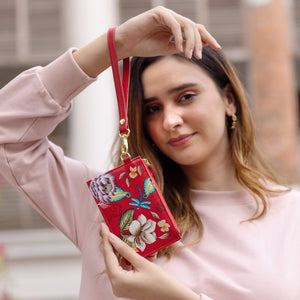 Woman holding a red floral Anuschka Card Holder with Wristlet - 1180 with RFID protection outdoors.