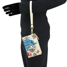 Load image into Gallery viewer, Person in a black outfit with an Anuschka Card Holder with Wristlet - 1180, RFID protected peacock-themed phone case with a shoulder strap.
