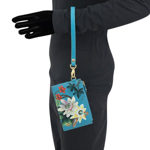 Person wearing a black outfit holding a blue floral-patterned Anuschka Card Holder with Wristlet - 1180.
