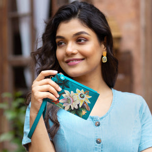 A woman smiling gently, holding a Anuschka Card Holder with Wristlet - 1180 with a genuine leather exterior.