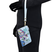 A person in a black outfit holds a light blue Anuschka Card Holder with Wristlet - 1180 featuring a colorful sea turtle design and a convenient wristlet strap.