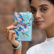 A person holds an Anuschka Card Holder with Wristlet - 1180 close to their face while wearing a white shirt.