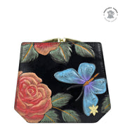 A black leather handbag with embossed red roses and a blue butterfly design, featuring a brass clasp closure and a "Genuine Leather" label in the top right corner, pairs exquisitely with the Anuschka Two Fold French Wallet - 1181 for a cohesive, stylish look.