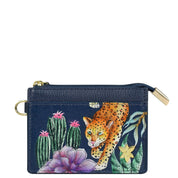 An Anuschka CARD CASE - 1183, a genuine leather navy blue wallet with a zipper, showcases a hand painted design of a jaguar, cacti, and flowers. The wallet features RFID protection and includes a ring attachment on one side.