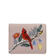 The Card Organizer Wallet - 1184 by Anuschka is a genuine leather wallet, showcasing a delicate red bird perched on a branch adorned with pink, yellow, and white flowers. This stunning piece features hand-painted artwork and serves as an elegant credit card holder.