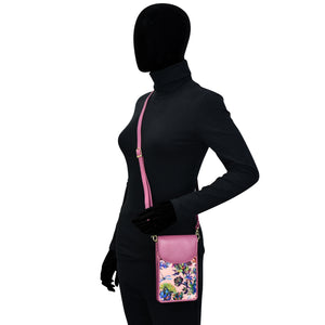 Mannequin displaying a black outfit with a pink floral Anuschka fabric with leather trim cell phone crossbody wallet featuring RFID protection.