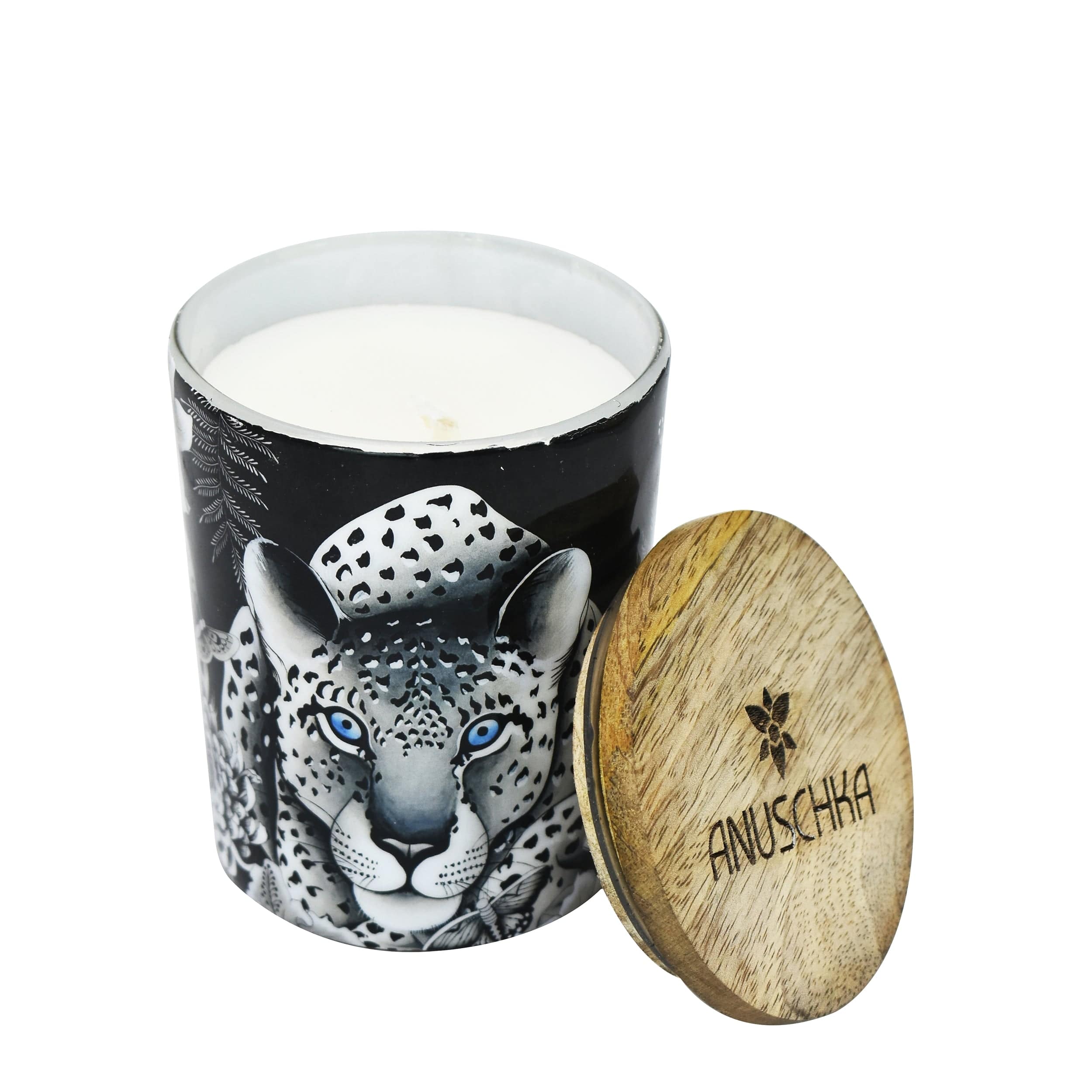 A luxurious Printed Glass Candle Jar - 25005 in a decorative black holder with a leopard design, placed beside a wooden lid with "Anuschka" engraved on it, capturing elegance at its finest.