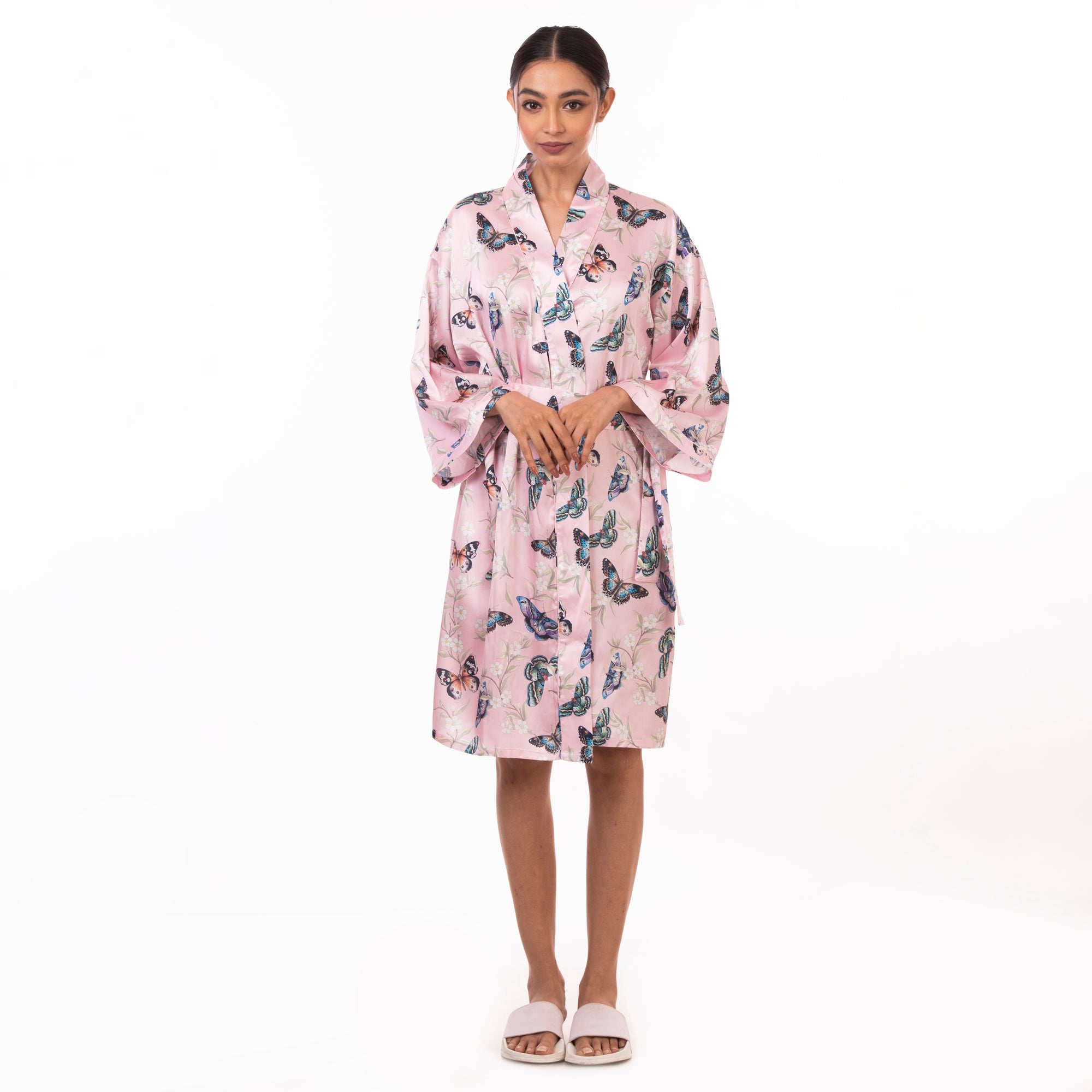 A person practicing self-care, standing against a white background, wearing a pink Anuschka 3343 robe with a bird pattern and white sandals.