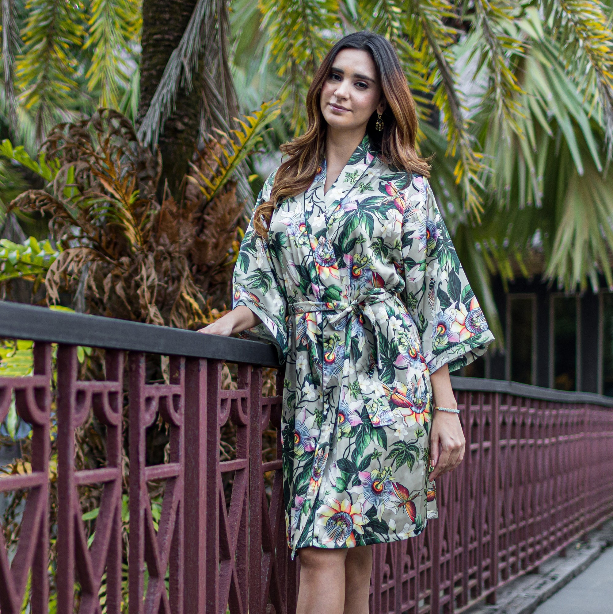 Woman posing in a Anuschka slip dress by a park railing.