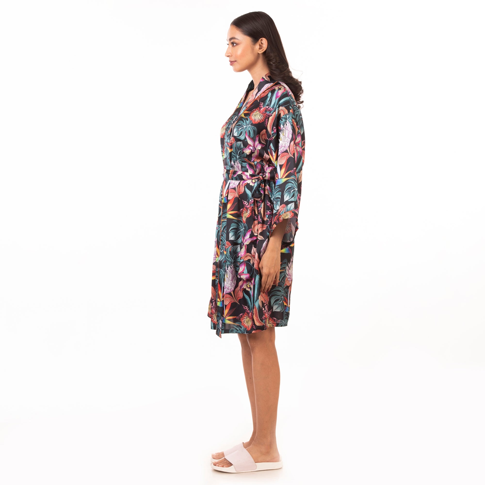 Woman standing sideways wearing a Anuschka 3343 tropical print silk robe and white sandals.