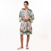 A woman modeling a silky floral Anuschka robe and white sandals against a white background, perfect for a self-care spa day.