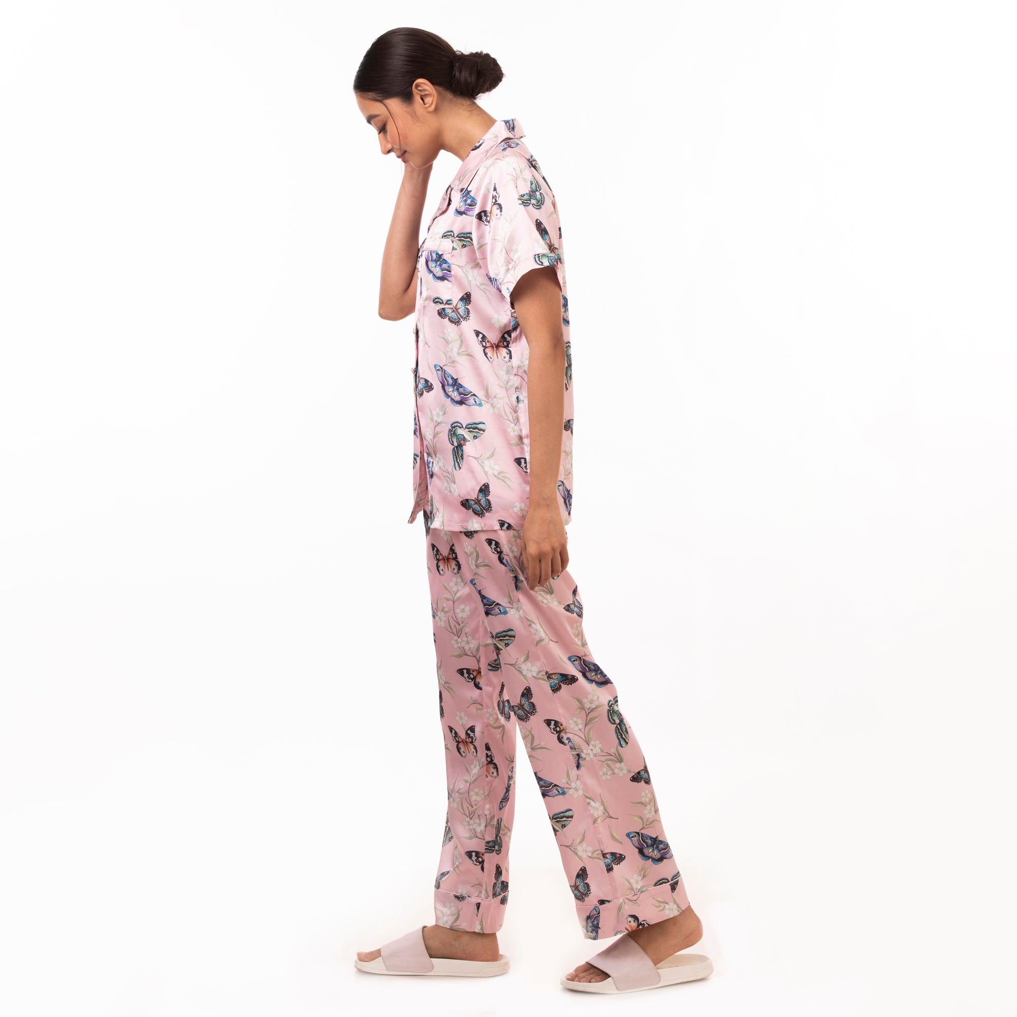 A person in a matching pink, Anuschka pajama set - 3344 with an original artwork pattern on the shirt and trousers, viewed from the side against a white background.