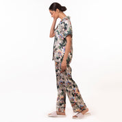 A woman in an Anuschka Pajama Set - 3344 with a floral print, made from recycled fabric, walking to the right with her head bowed down.