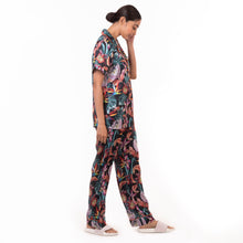 Load image into Gallery viewer, A woman in an Anuschka pajama set - 3344 featuring recycled fabric, glancing down with her hand near her face.
