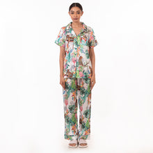Load image into Gallery viewer, A woman stands facing the camera, wearing an Anuschka tropical print pajama set with a relaxed fit, made from recycled fabric.
