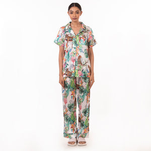 A woman stands facing the camera, wearing an Anuschka tropical print pajama set with a relaxed fit, made from recycled fabric.