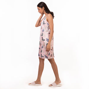 A woman in a floral slip dress made of recycled polyester by Anuschka, style 3346, walking against a white background, featuring adjustable shoulder straps.