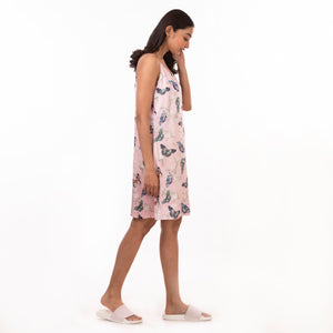 Woman in a floral Anuschka slip dress made of recycled polyester, standing sideways to the camera with adjustable shoulder straps visible.