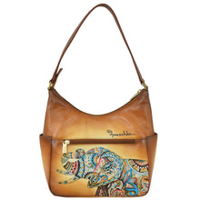 Load image into Gallery viewer, The Classic Hobo With Side Pockets - 382 by Anuschka features a genuine leather handbag accented with a hand-painted, colorful, patterned rhino design on the front pocket and an adjustable shoulder strap. The brand name &quot;Anuschka&quot; is printed prominently above the design.
