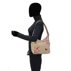 Side profile of a person with a blacked-out face carrying an Anuschka Classic Hobo With Side Pockets - 382 handbag with a shoulder strap over their shoulder.