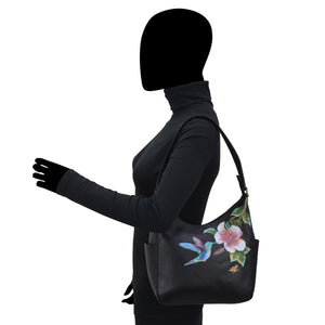 Woman in a black turtleneck showcasing a Anuschka Classic Hobo With Side Pockets - 382 handbag with floral embroidery on the shoulder strap.