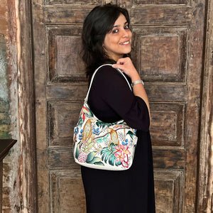 Woman smiling and posing with an Anuschka Classic Hobo With Side Pockets - 382 handbag, featuring a shoulder strap, in front of a rustic wooden door.