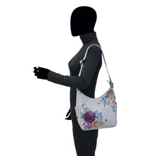 Load image into Gallery viewer, Woman with obscured face, wearing a gray top and carrying an Anuschka Classic Hobo With Studded Side Pockets - 433 shoulder bag with an adjustable shoulder strap.
