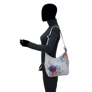 Woman with obscured face, wearing a gray top and carrying an Anuschka Classic Hobo With Studded Side Pockets - 433 shoulder bag with an adjustable shoulder strap.