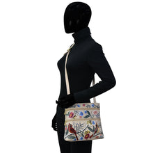 Load image into Gallery viewer, Mannequin displaying a black leather outfit with a floral print shoulder bag featuring an adjustable shoulder strap, the Anuschka Medium Crossbody With Double Zip Pockets - 447.
