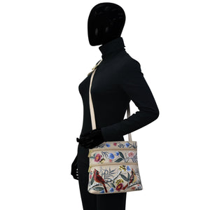 Mannequin displaying a black leather outfit with a floral print shoulder bag featuring an adjustable shoulder strap, the Anuschka Medium Crossbody With Double Zip Pockets - 447.