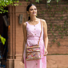 Load image into Gallery viewer, A woman in a pink sleeveless dress with an Anuschka Medium Crossbody With Double Zip Pockets - 447 featuring an adjustable shoulder strap walking outdoors.
