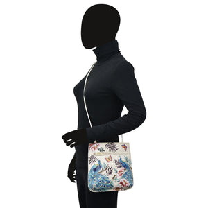A silhouette of a person wearing a turtleneck and carrying a dark forest green, floral-patterned Anuschka Slim Crossbody With Front Zip - 452 made of genuine leather.