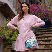 Load image into Gallery viewer, Woman in a pink dress with an Anuschka genuine leather Slim Crossbody With Front Zip - 452 standing confidently on stairs with blooming flowers in the background.
