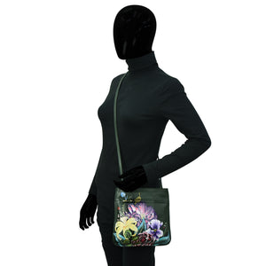 Mannequin with black head and dark gray outfit, wearing gloves and carrying an Anuschka Slim Crossbody With Front Zip - 452 in a floral print design.