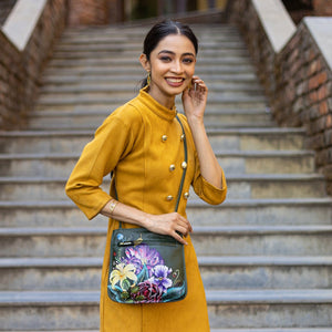 A woman in a yellow outfit with a hand-painted, Anuschka Slim Crossbody With Front Zip - 452 genuine leather mini crossbody purse smiles on steps.