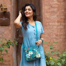 Load image into Gallery viewer, A woman in a blue dress smiling and holding a floral, genuine leather Anuschka Expandable Travel Crossbody - 550.
