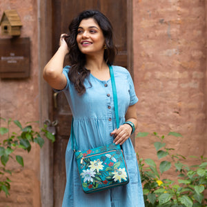 A woman in a blue dress smiling and holding a floral, genuine leather Anuschka Expandable Travel Crossbody - 550.