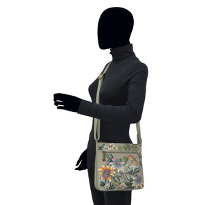 Mannequin displaying an Anuschka Expandable Travel Crossbody - 550 with floral design and an adjustable strap.