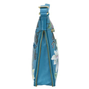 Side view of a blue floral print, genuine leather Anuschka handbag with a zipper closure.