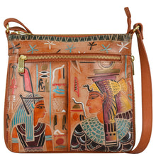 Load image into Gallery viewer, The Anuschka Expandable Travel Crossbody - 550 is crafted from genuine leather and showcases an ancient Egyptian-inspired design with two figures depicted in colorful traditional attire amidst hieroglyphic motifs. The hand-painted artwork is complemented by a front zipper pocket and an adjustable strap.
