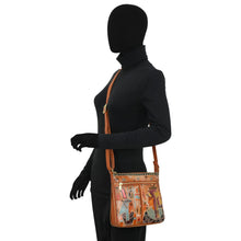 Load image into Gallery viewer, A mannequin dressed in black holds the Anuschka Expandable Travel Crossbody - 550 in tan genuine leather, featuring abstract, colorful hand-painted artwork.
