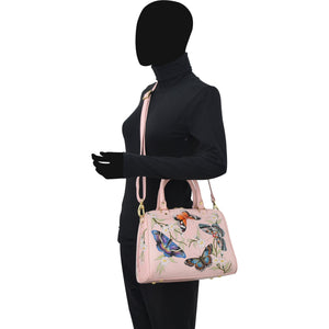 A mannequin displaying an Anuschka Zip Around Classic Satchel - 625 with hand-painted butterfly motifs, dressed in a black turtleneck and trousers.