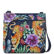 The Anuschka Crossbody With Front Zip Organizer - 651 features a colorful, hand-painted leather design with leopards, large flowers, and butterflies on a dark navy background. This bag includes an RFID protected organizer, a front pocket, and an adjustable shoulder strap.