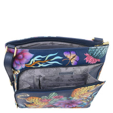 Load image into Gallery viewer, The Anuschka Crossbody With Front Zip Organizer - 651 is a blue hand-painted leather handbag adorned with a unique floral and leopard print design. Inside, you&#39;ll find a grey interior featuring multiple pockets, intricate patterns, and an RFID protected organizer. For added convenience, the bag includes an adjustable crossbody strap.
