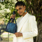 A woman in a white blazer posing with an Anuschka blue leather handbag.