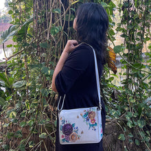 Load image into Gallery viewer, Woman with an Anuschka Flap Crossbody - 683 standing in front of green foliage.
