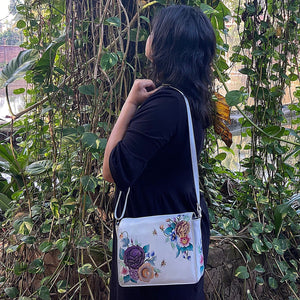 Woman with an Anuschka Flap Crossbody - 683 standing in front of green foliage.