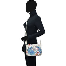 Load image into Gallery viewer, A person standing sideways wearing a black outfit and holding a hand painted Anuschka Flap Crossbody - 683 with a leather crossbody strap.
