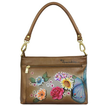 Load image into Gallery viewer, The Anuschka Shoulder Organizer - 684 is a genuine leather handbag with a single shoulder strap and a removable crossbody strap, featuring colorful flowers and a blue butterfly. This bag boasts gold-tone hardware, an external zip pocket, and RFID protection for added security.
