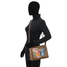 Load image into Gallery viewer, A faceless mannequin dressed in black wears an Anuschka Shoulder Organizer - 684, a genuine leather crossbody brown handbag featuring a colorful butterfly and flowers design.
